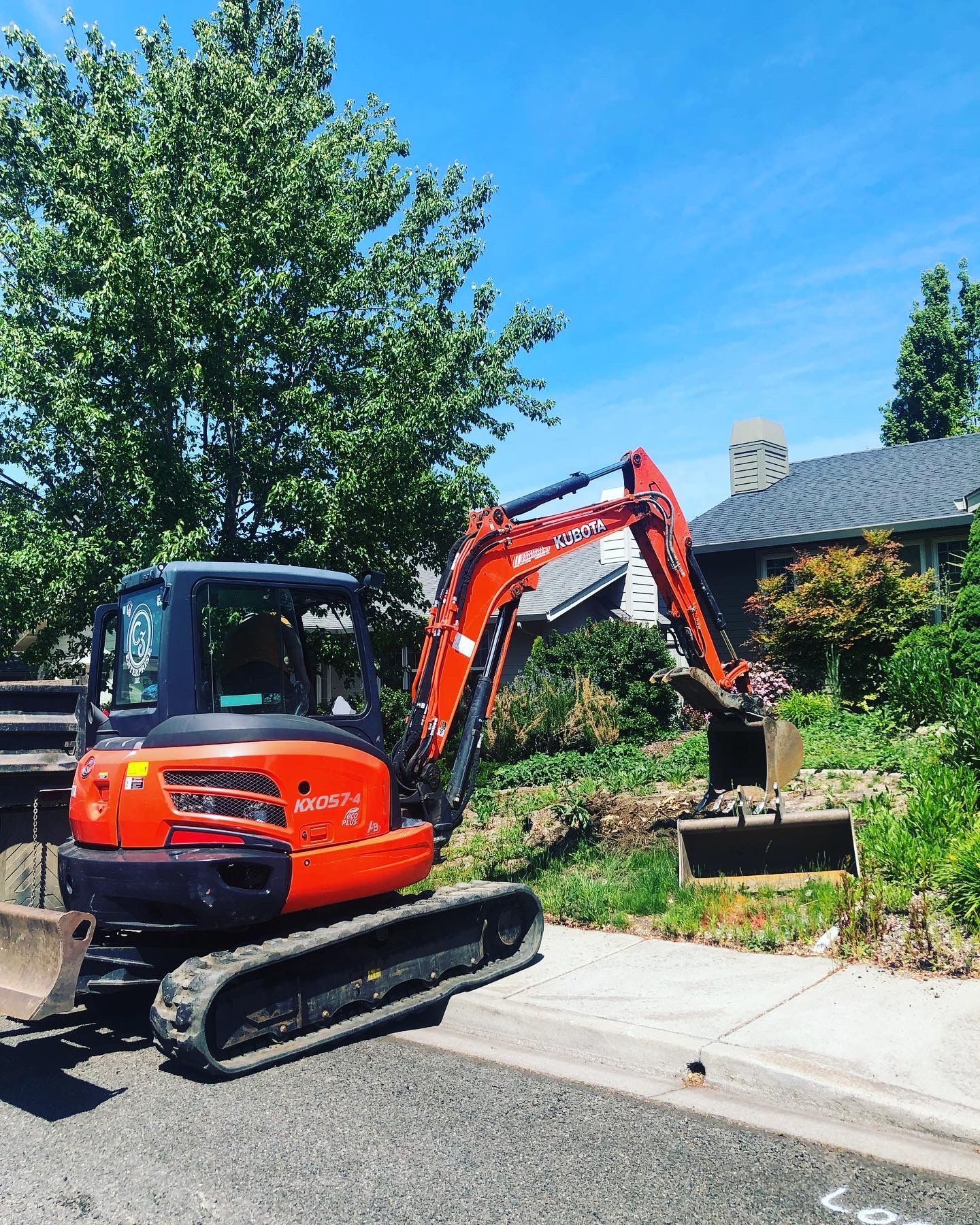 A red excavator is parked on the side of the road in front of a house.