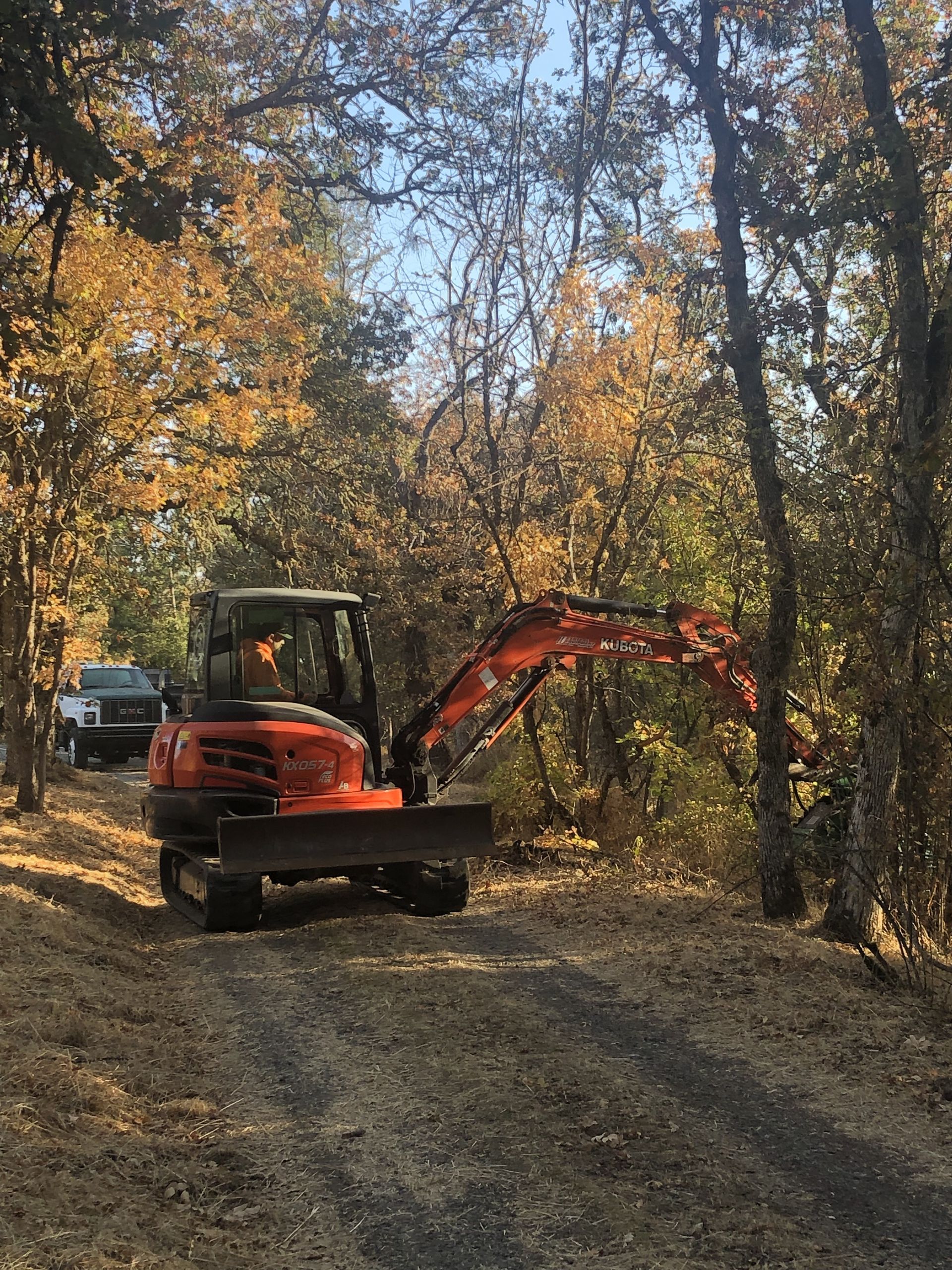 An excavator is driving down a dirt road in the woods.