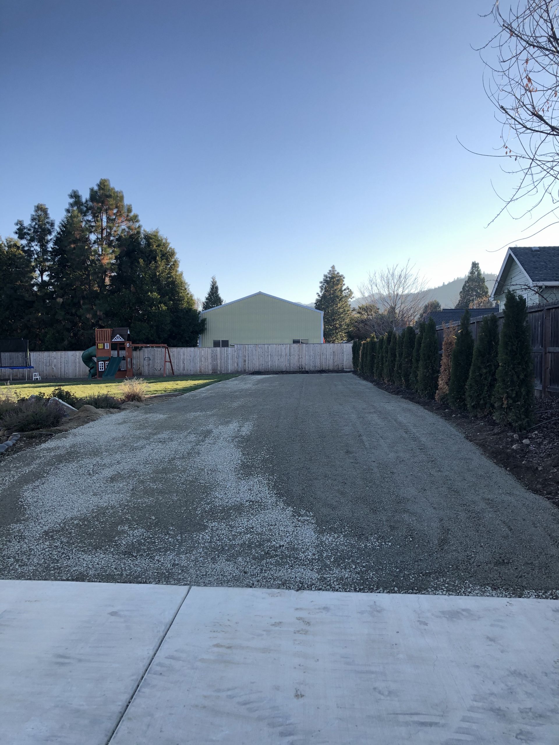 A gravel driveway with a fence and a house in the background.