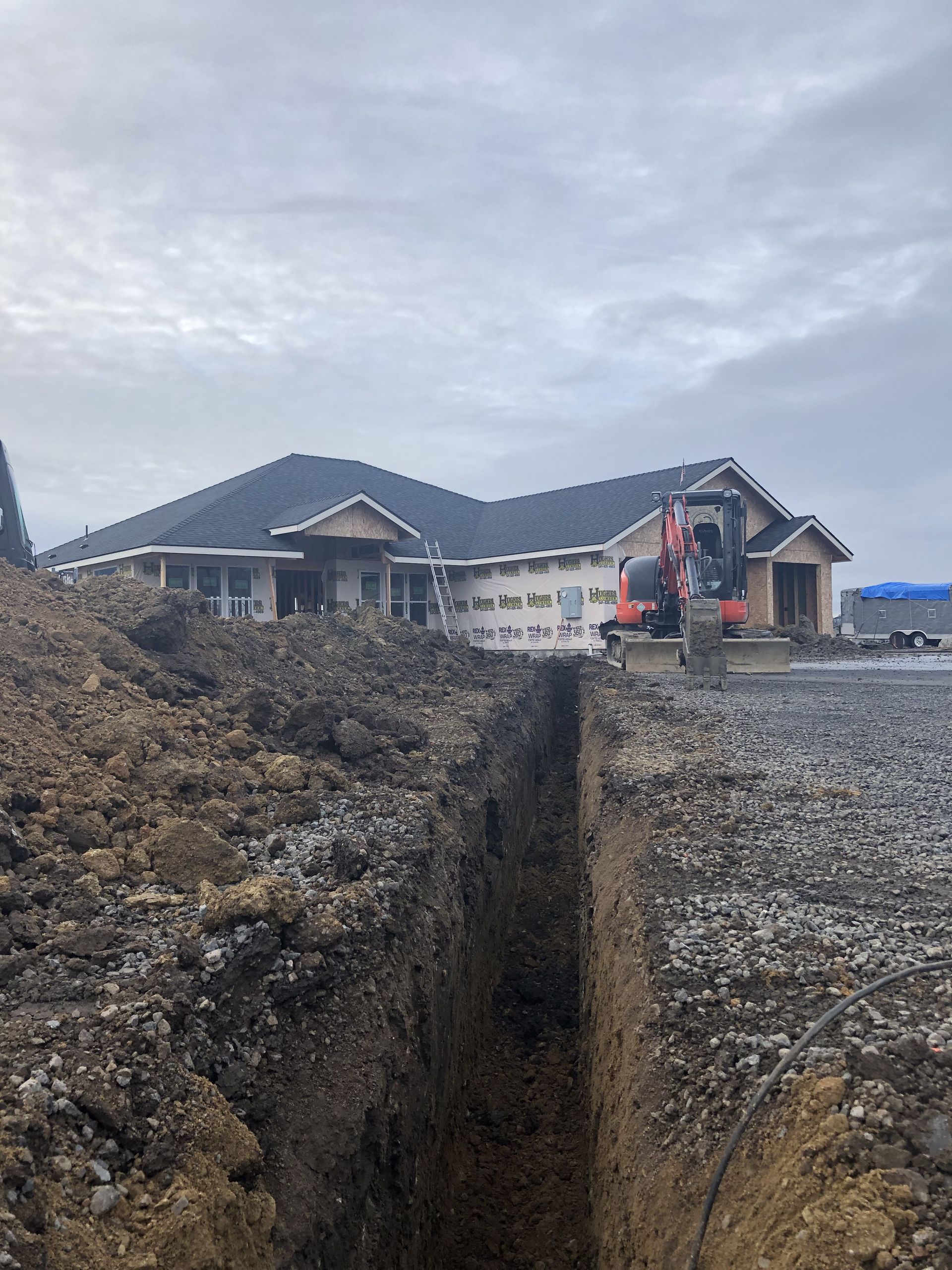 An excavator is digging a trench in front of a house.