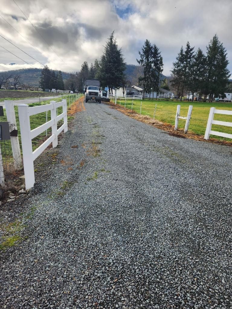 A gravel road with a white fence leading to a field.