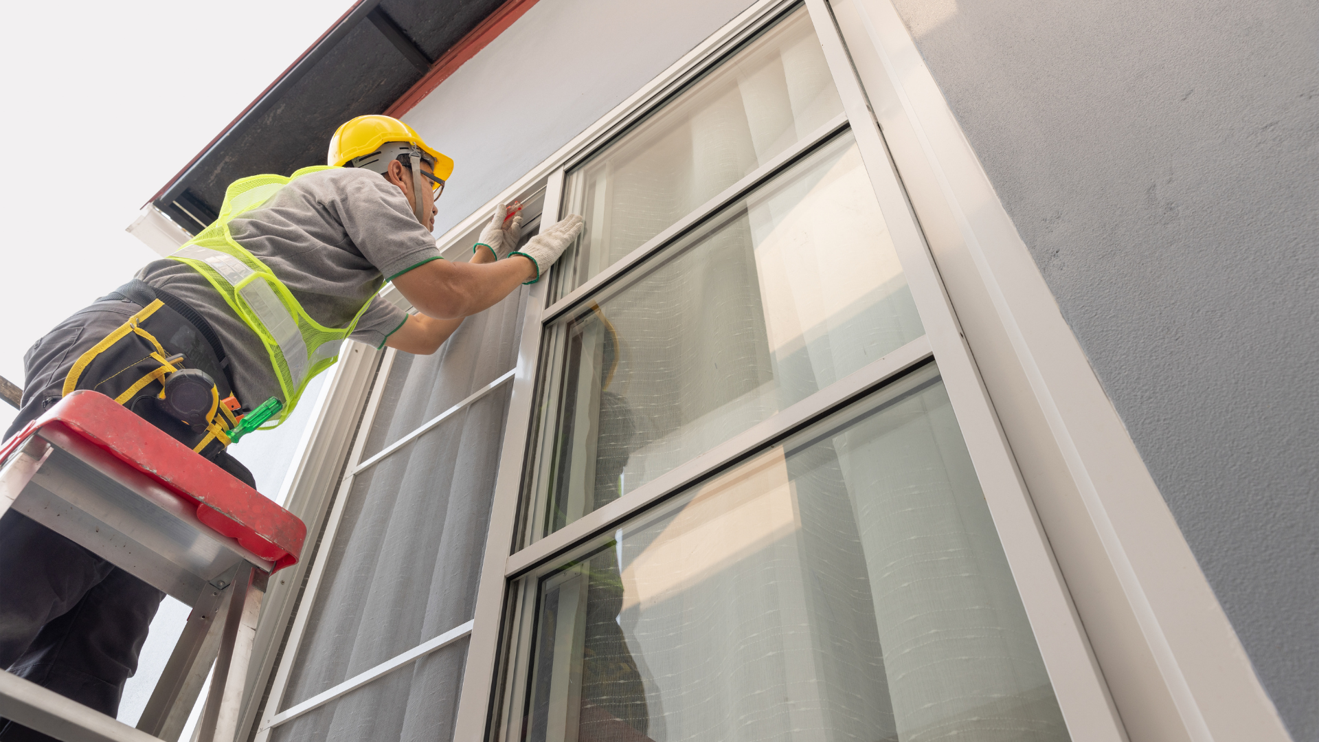 A man is standing on a ladder fixing a window.