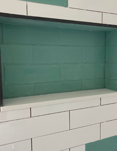A shelf is built into a brick wall with green tiles.