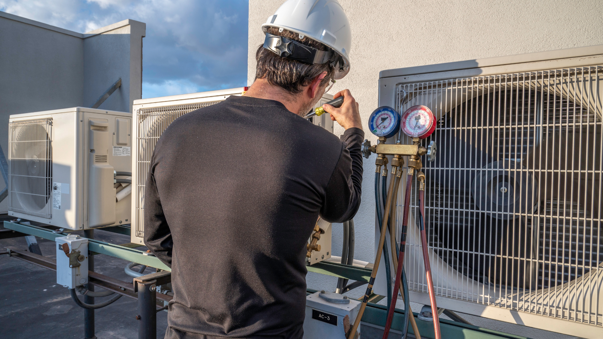 A man is working on an air conditioner on the roof of a building.