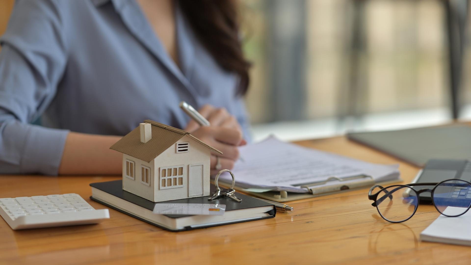 A woman is sitting at a desk with a model house and a pen.