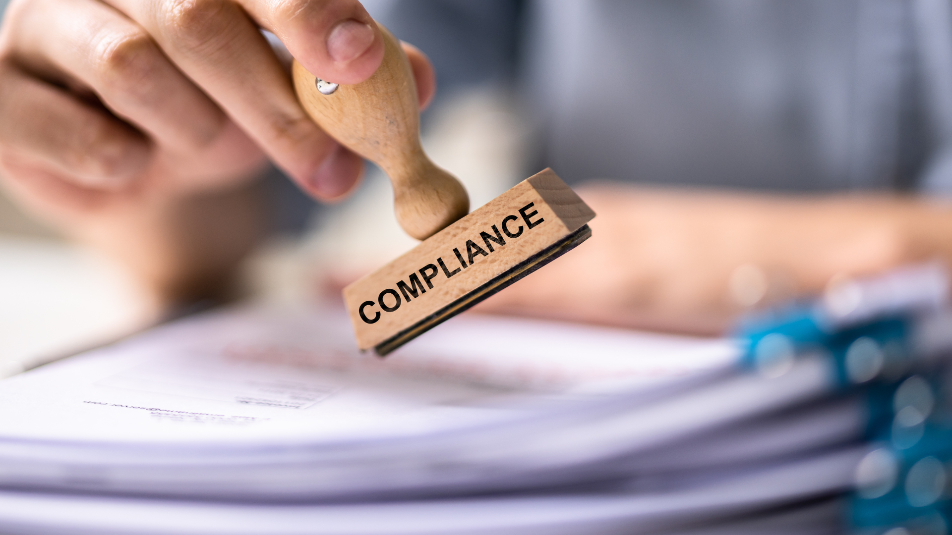 A person is stamping the word compliance on a piece of paper.