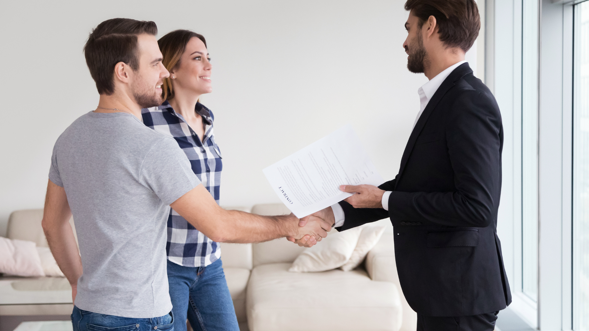 A man in a suit is shaking hands with a couple in a living room.