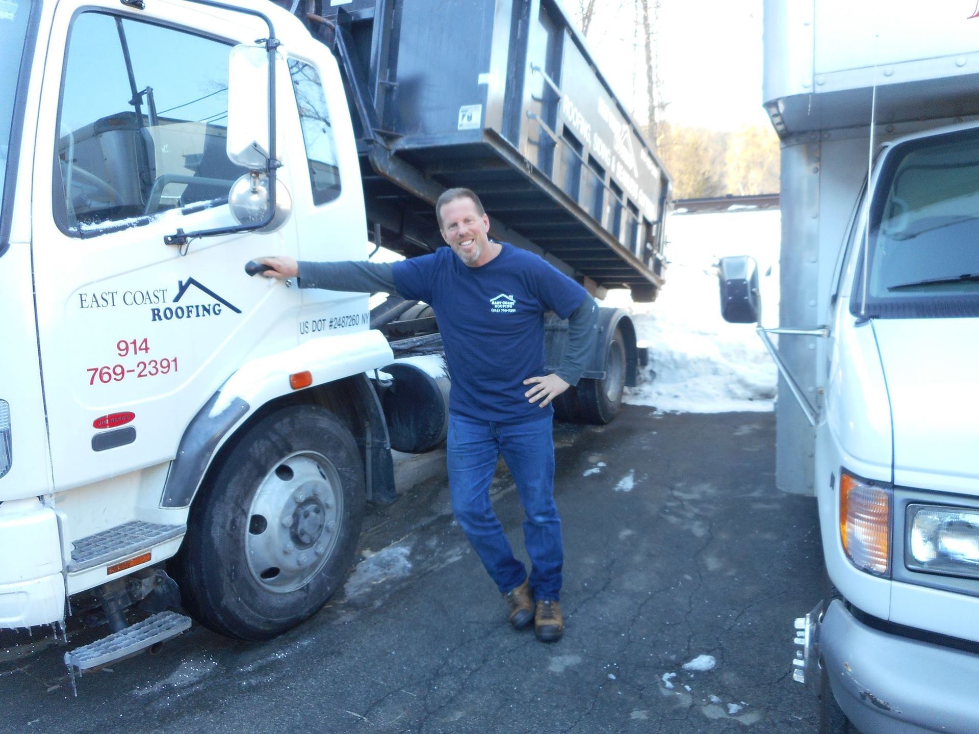 A man is standing in front of a dump truck with the number 7w5-2361 on it