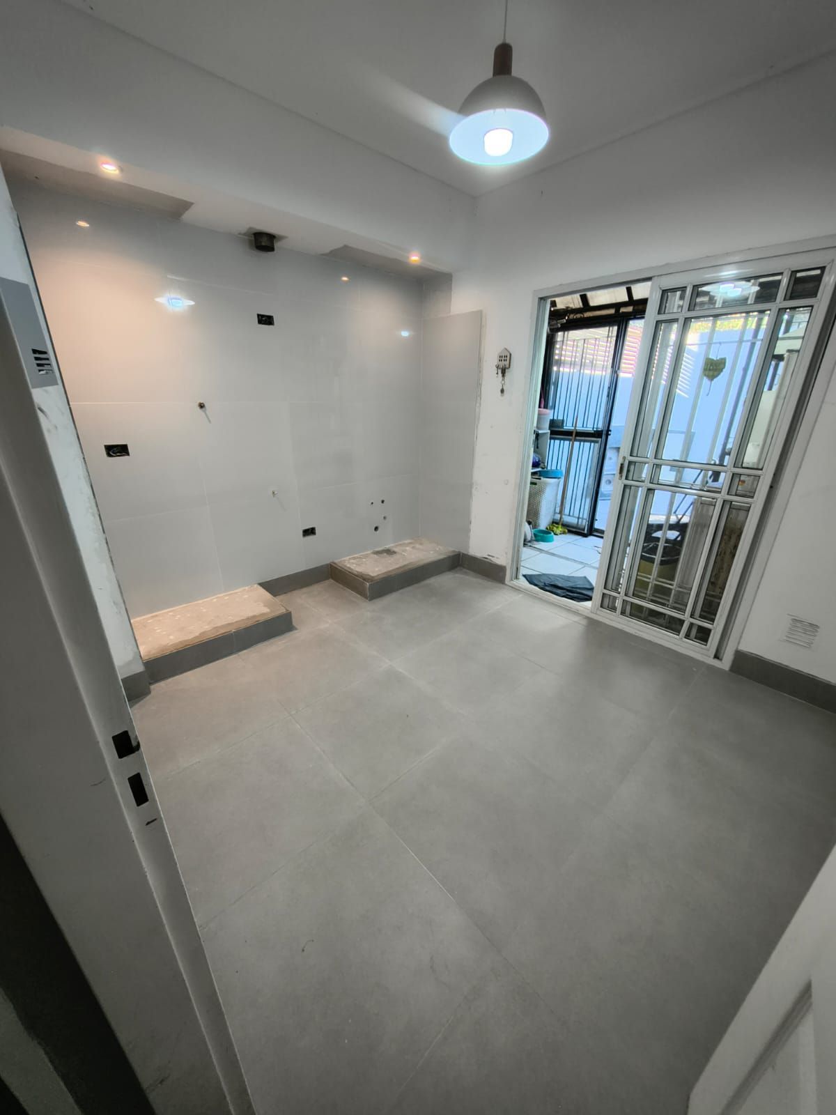 Habitación vacía con azulejos blancos, luces empotradas, puerta con ventana y soporte para ventilador de techo.
