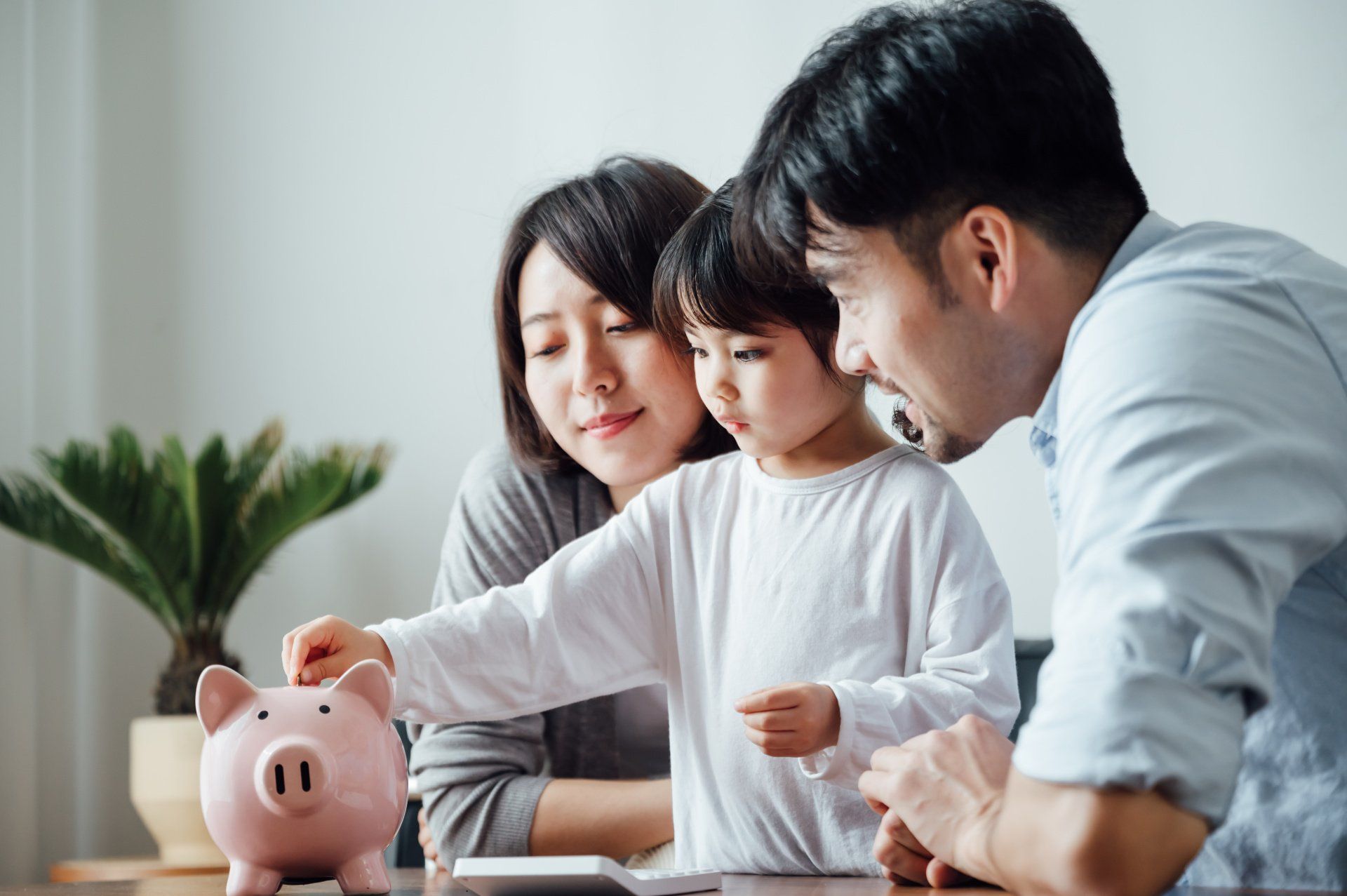 Two parents with kid putting money in piggy bank