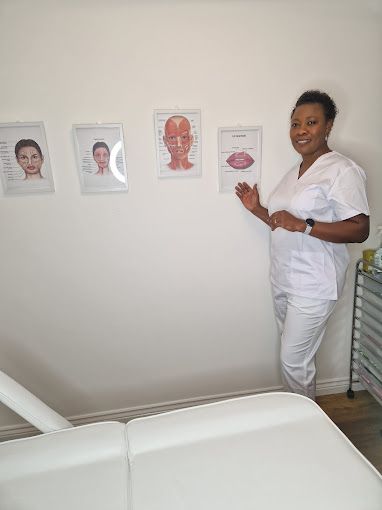 A woman in a white scrub is standing in front of a wall with pictures of faces on it.