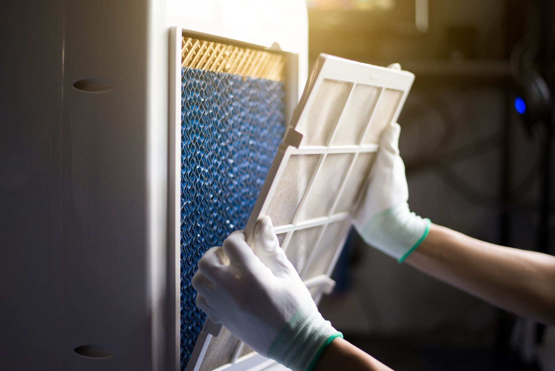 Hands in white gloves removing a dust filter from an air cooler, revealing a blue honeycomb cooling pad behind it.