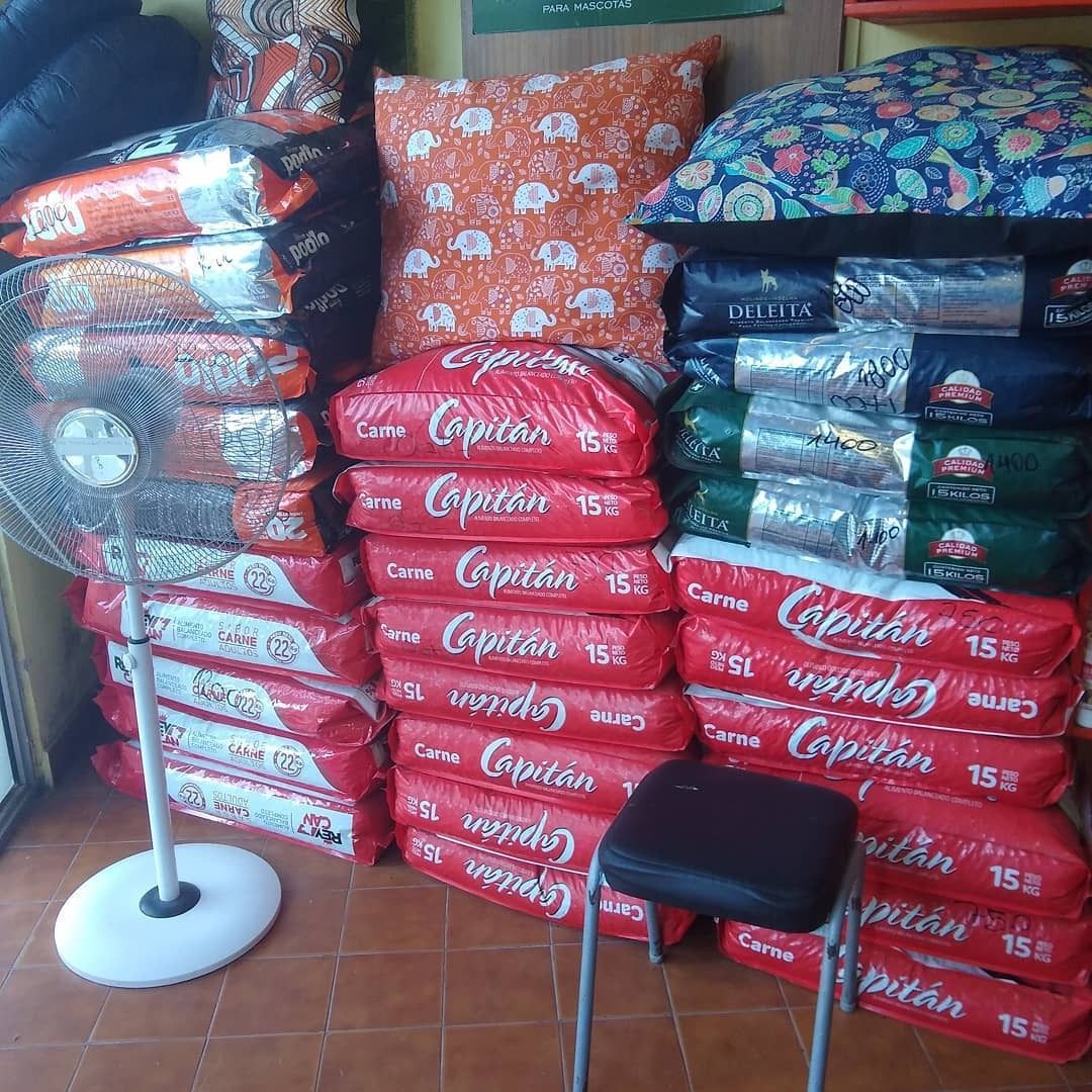 Interior de una tienda con pilas de bolsas rojas y cojines. También hay un taburete y un ventilador.