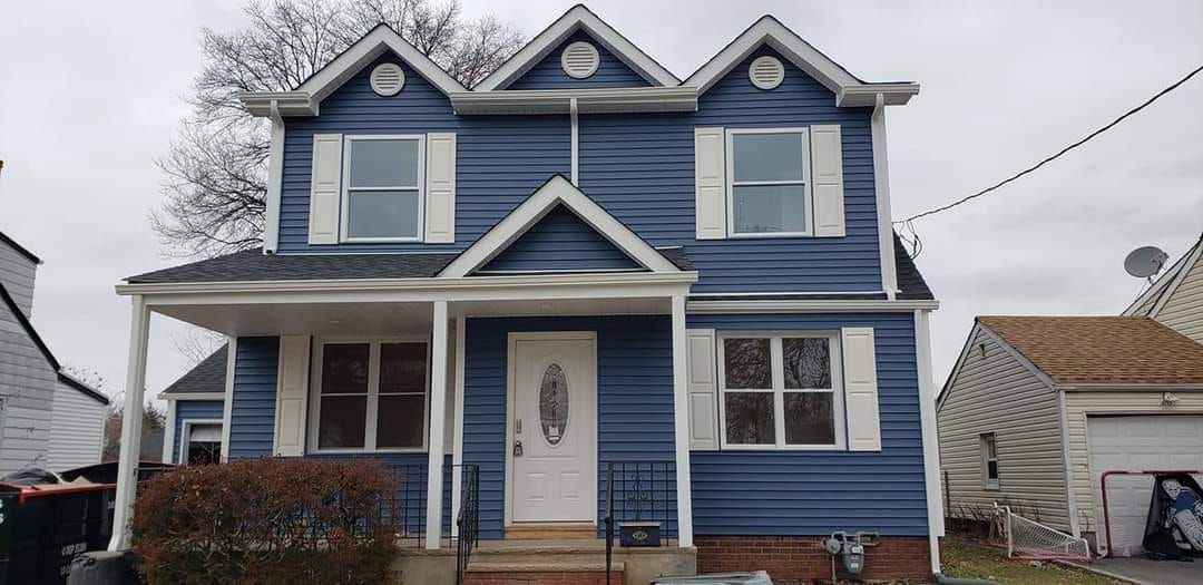 a blue house with white shutters and a porch on a cloudy day .
