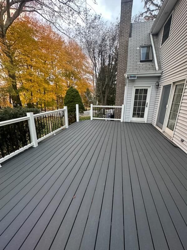 a large gray deck with a white railing is in front of a house .