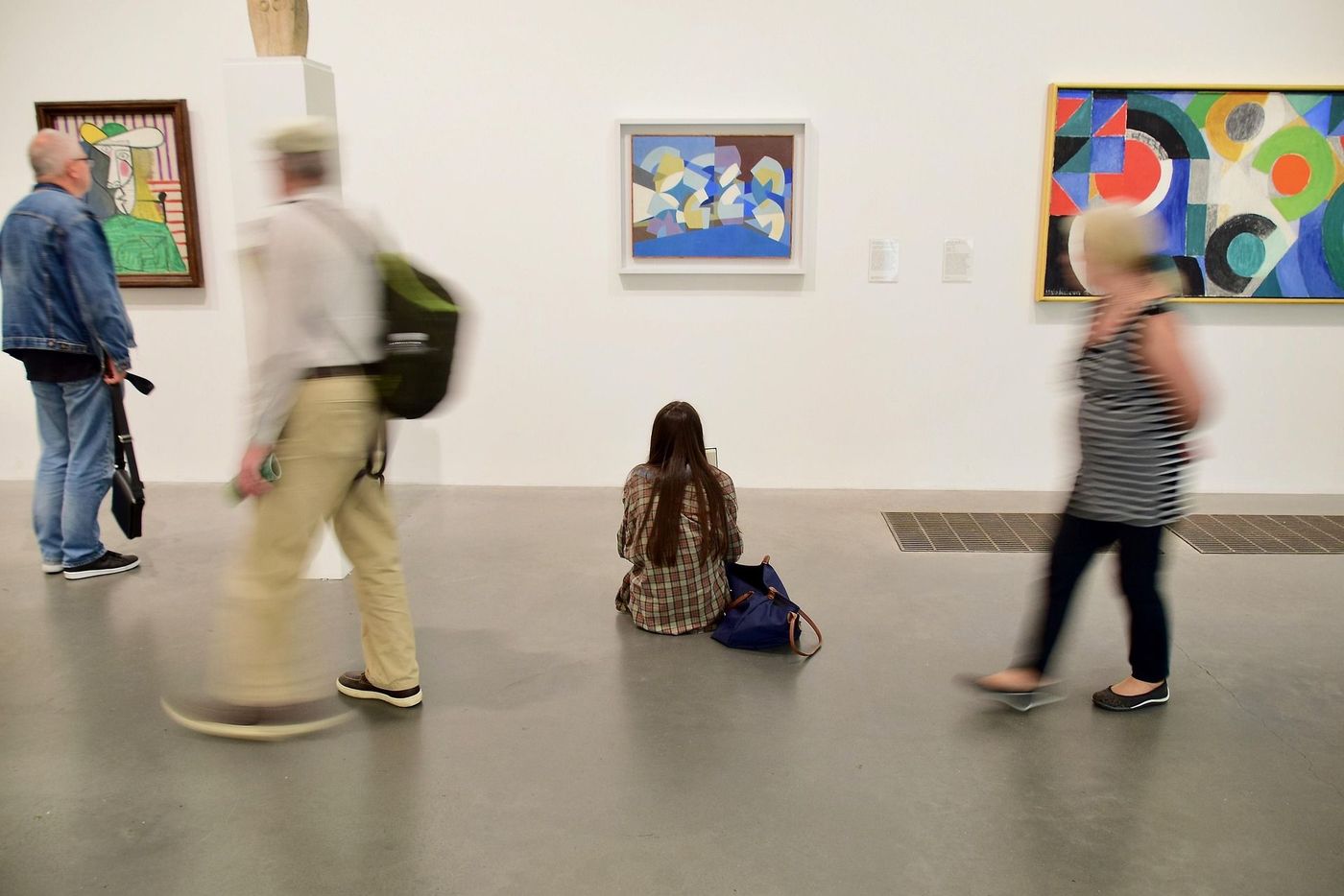drie personen die langs een muur met grafische kunst lopen, een vrouw zit op de grond, in het midden