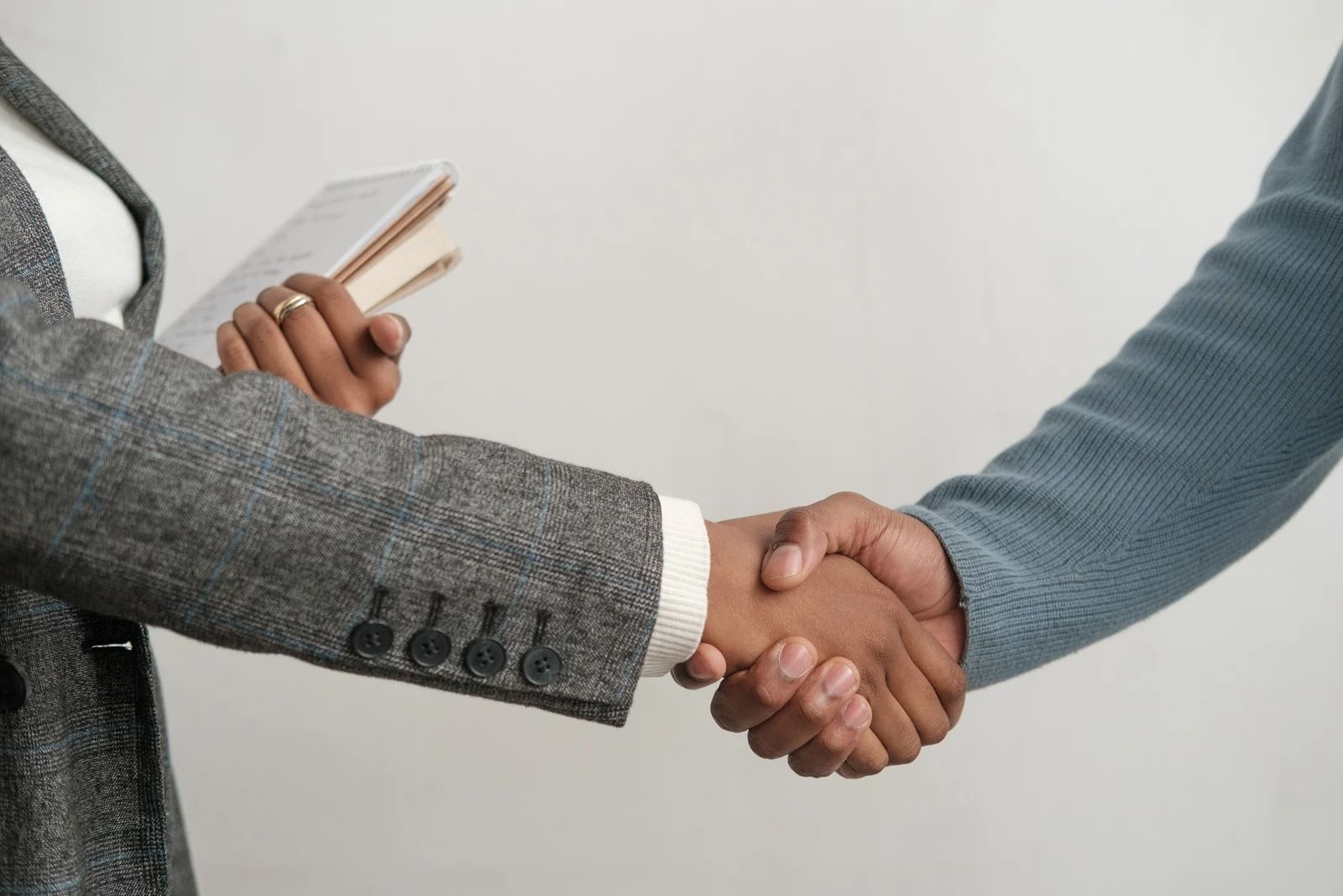 Two people in textured business-casual clothing shake hands against a plain white background.