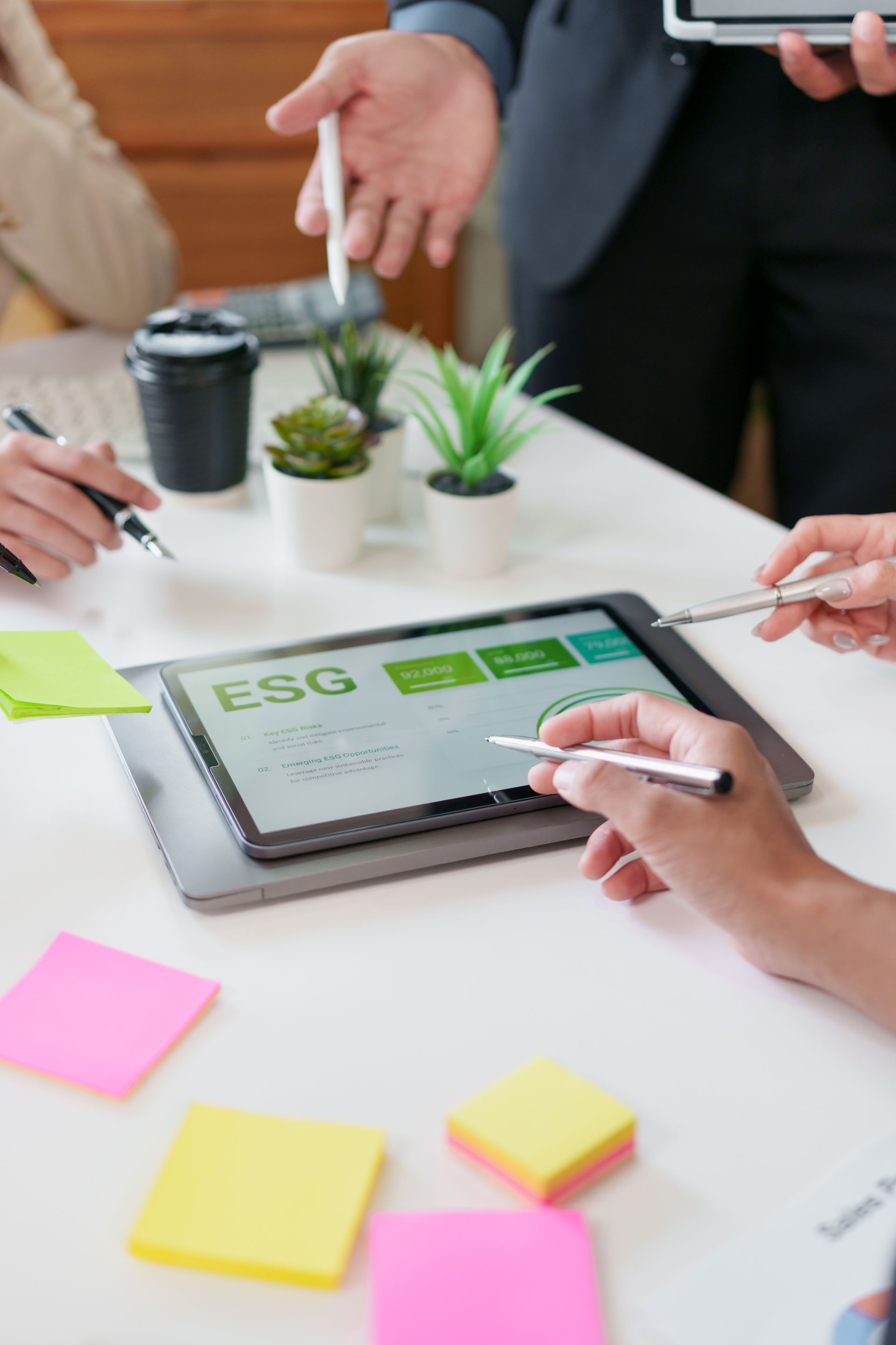 People in meeting reviewing ESG data on a tablet, surrounded by sticky notes and plants.