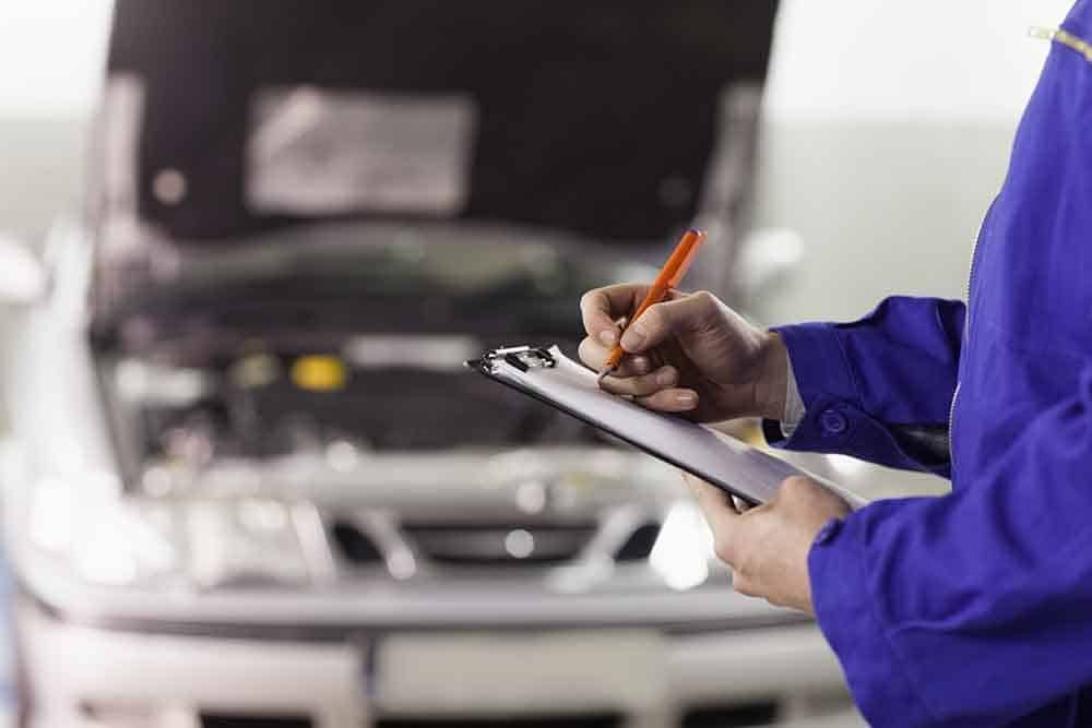 A Mechanic Is Writing On A Clipboard In Front Of A Car — Signature Mechanical In South Gladstone, QLD