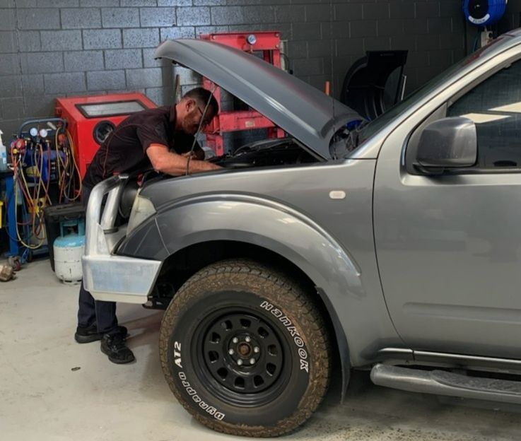 Mechanic working under the hood of a car in an auto repair shop, inspecting and repairing the engine