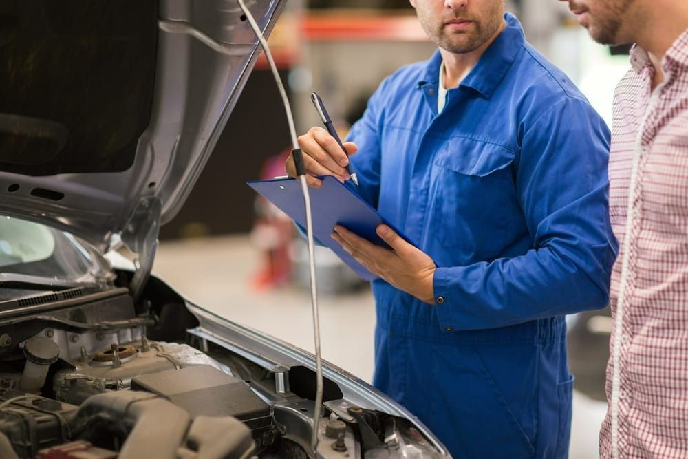 A Mechanic Is Looking Under The Hood Of A Car While A Man Looks On — Signature Mechanical In South Gladstone, QLD