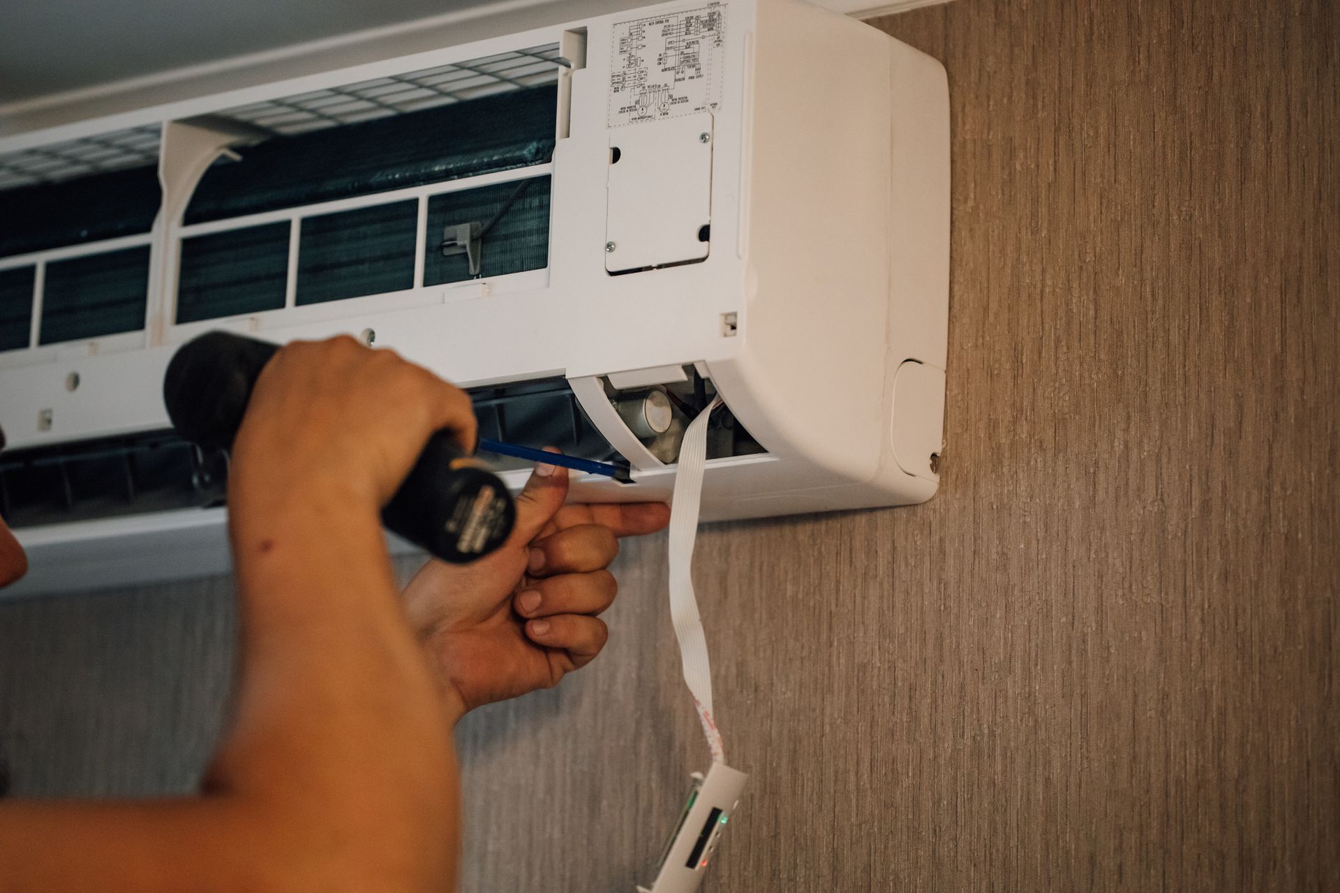 Technician performing residential air conditioning repair on a wall-mounted unit with a screwdriver.