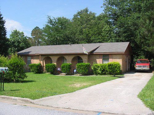 Brick ranch house with arched entry and red truck parked in the driveway. Green lawn and bushes in front.