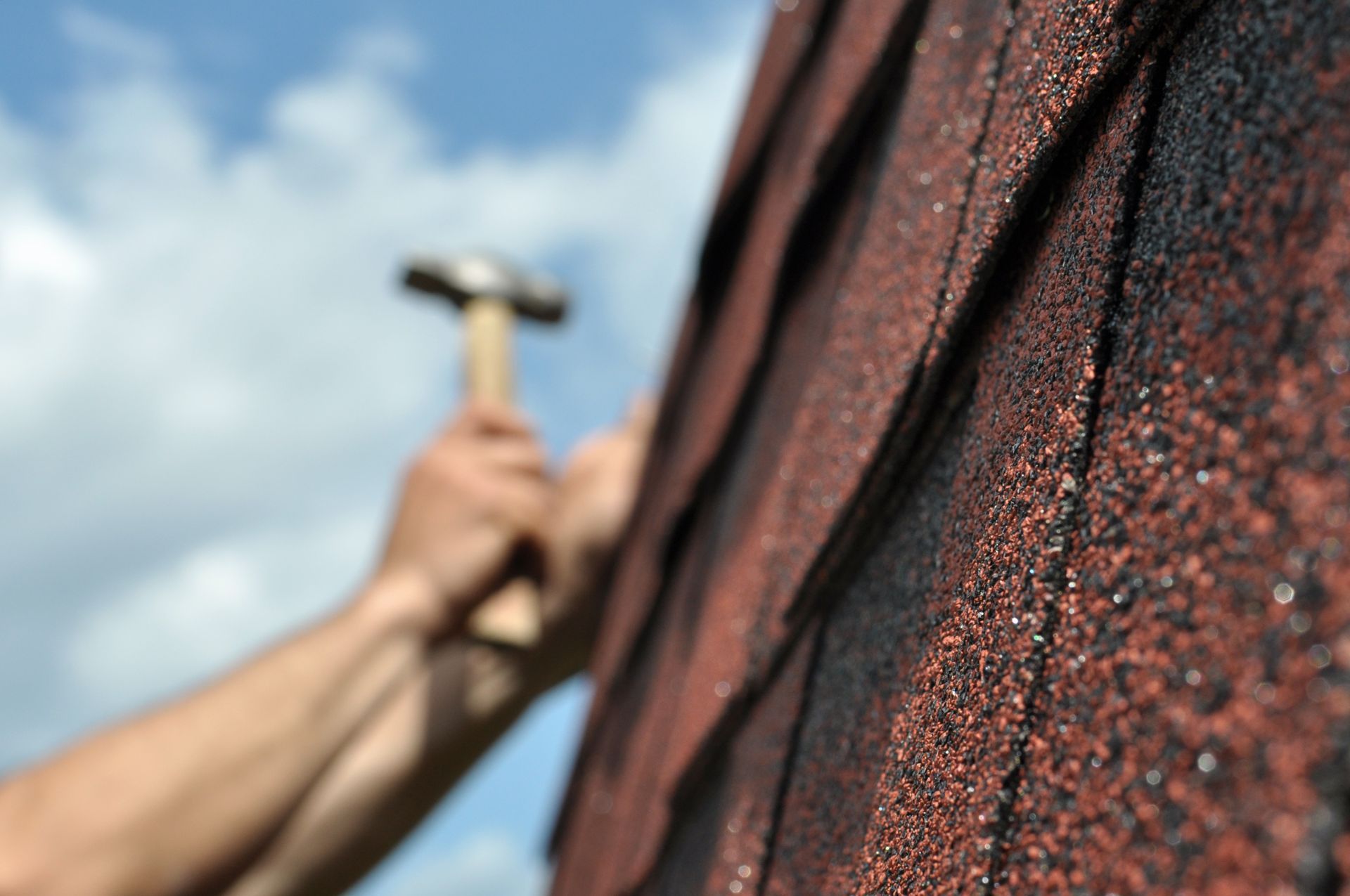 Closeup of roof tiles, with blurry hands residential roofer’s hands holding a hammer.