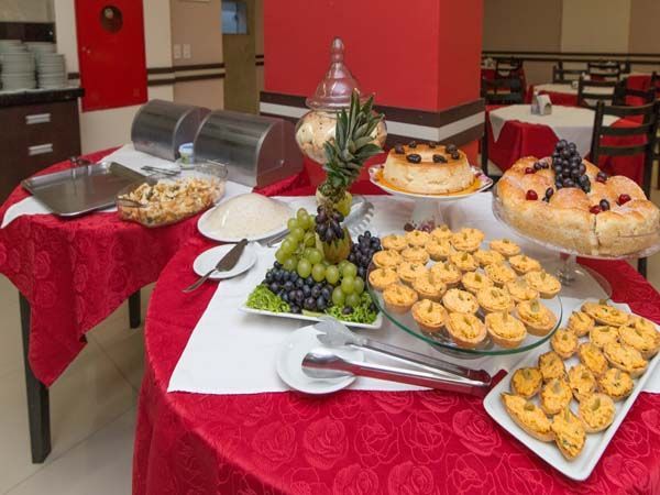 Mesa de bufê com diversas sobremesas, frutas e doces sobre toalhas de mesa vermelhas.