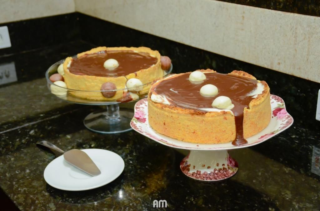 Dois cheesecakes de chocolate em suportes decorativos para bolos, com uma espátula de servir sobre um prato.