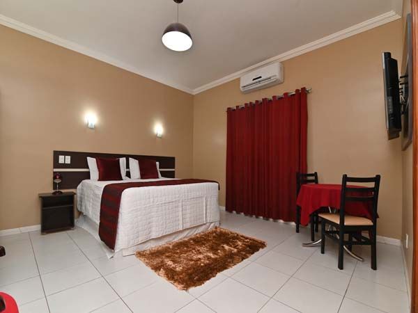 Quarto com cama, mesa e cadeiras. Detalhes em vermelho e ar condicionado visíveis.