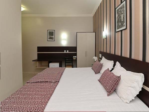 Quarto de hotel com cama, escrivaninha, guarda-roupa e parede com detalhes listrados.