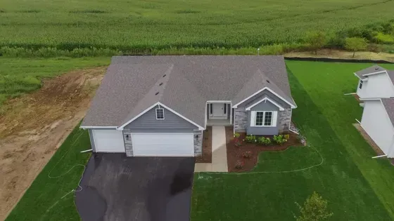 Aerial view of a light blue house with a gray roof, stone accents, and two-car garage on green grass.