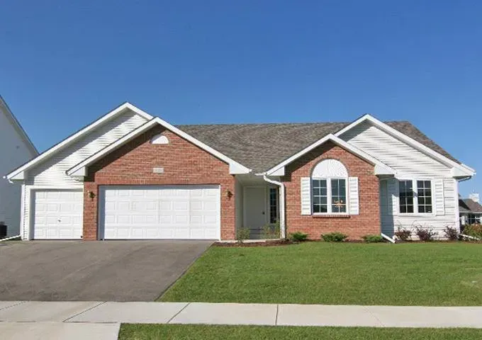 Brick and white-sided house with two-car garage, green lawn, and blue sky.