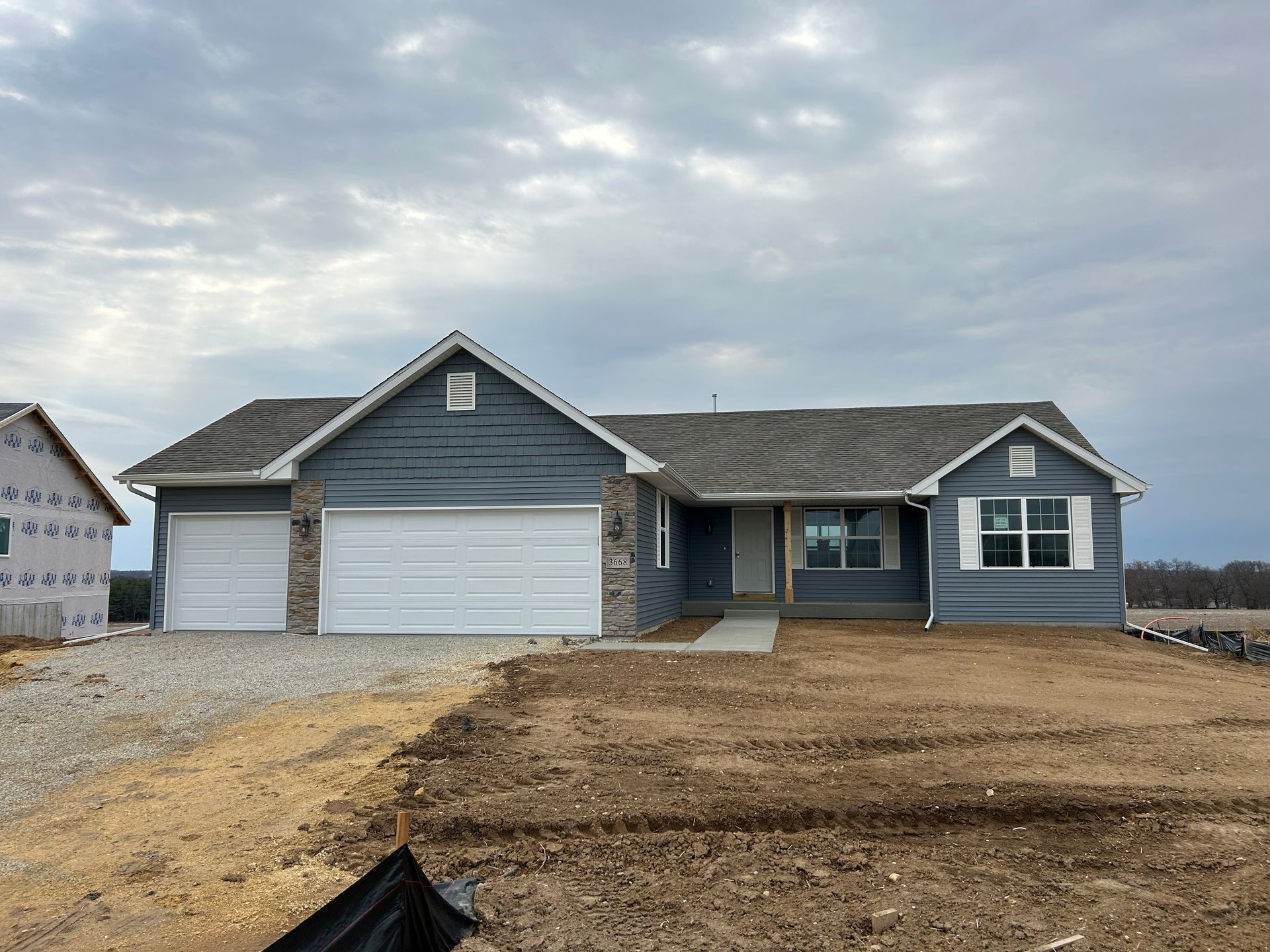 New construction house, blue siding, stone garage accents, gray roof, cloudy sky.