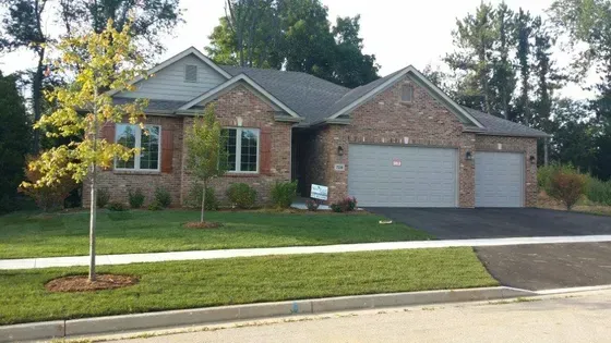 Brick home with a two-car garage and manicured lawn. A tree in the front yard.