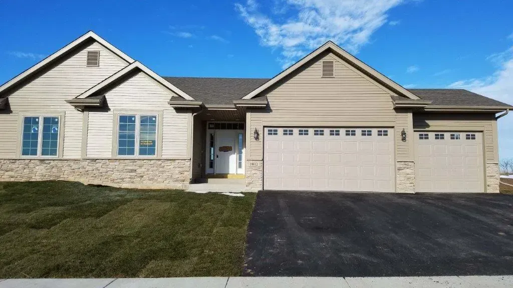 Tan ranch-style house with two-car garage on a sunny day. Stone accents, asphalt driveway.