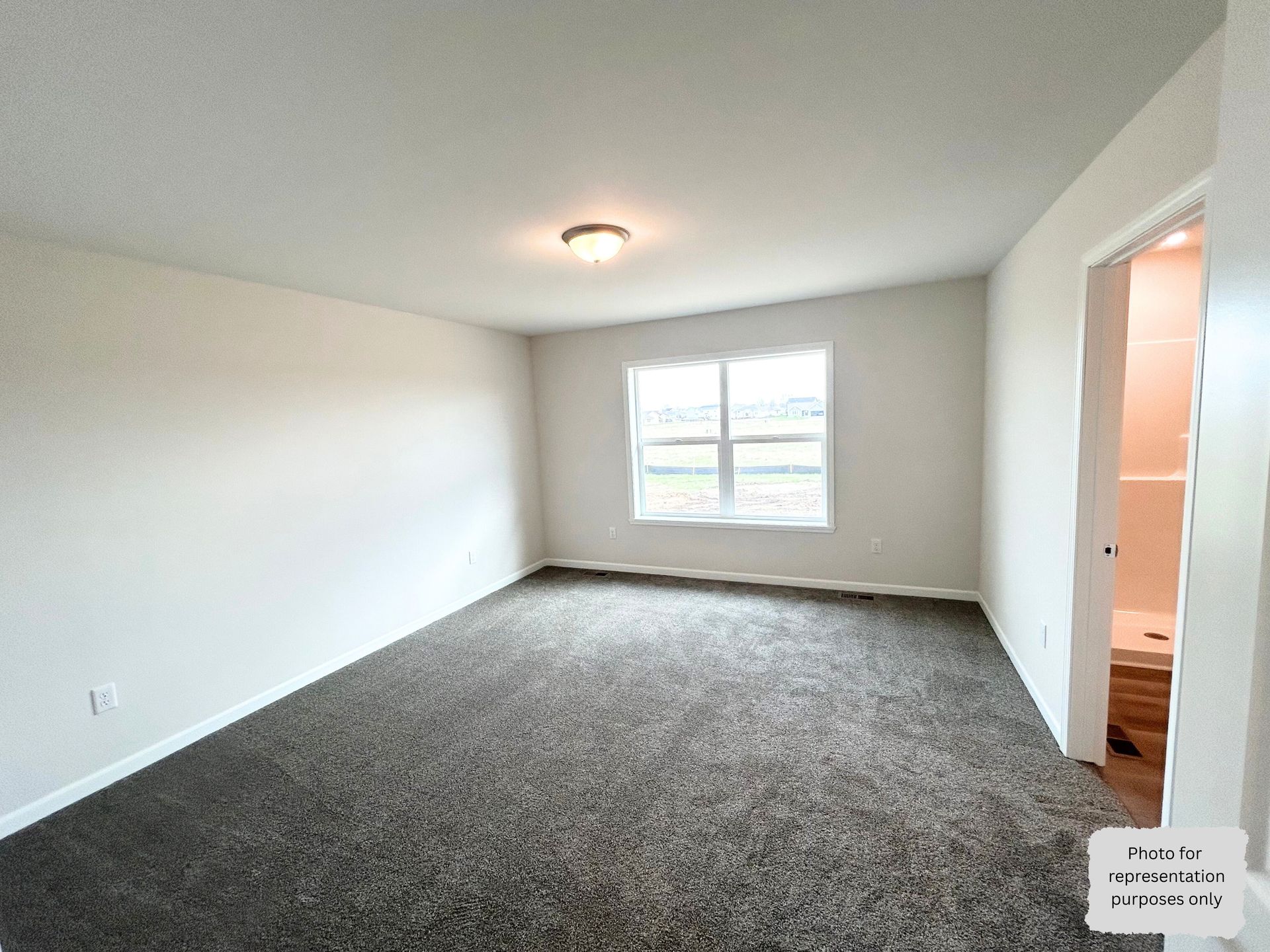Empty bedroom with grey carpet, white walls, window, and open door to a bathroom.