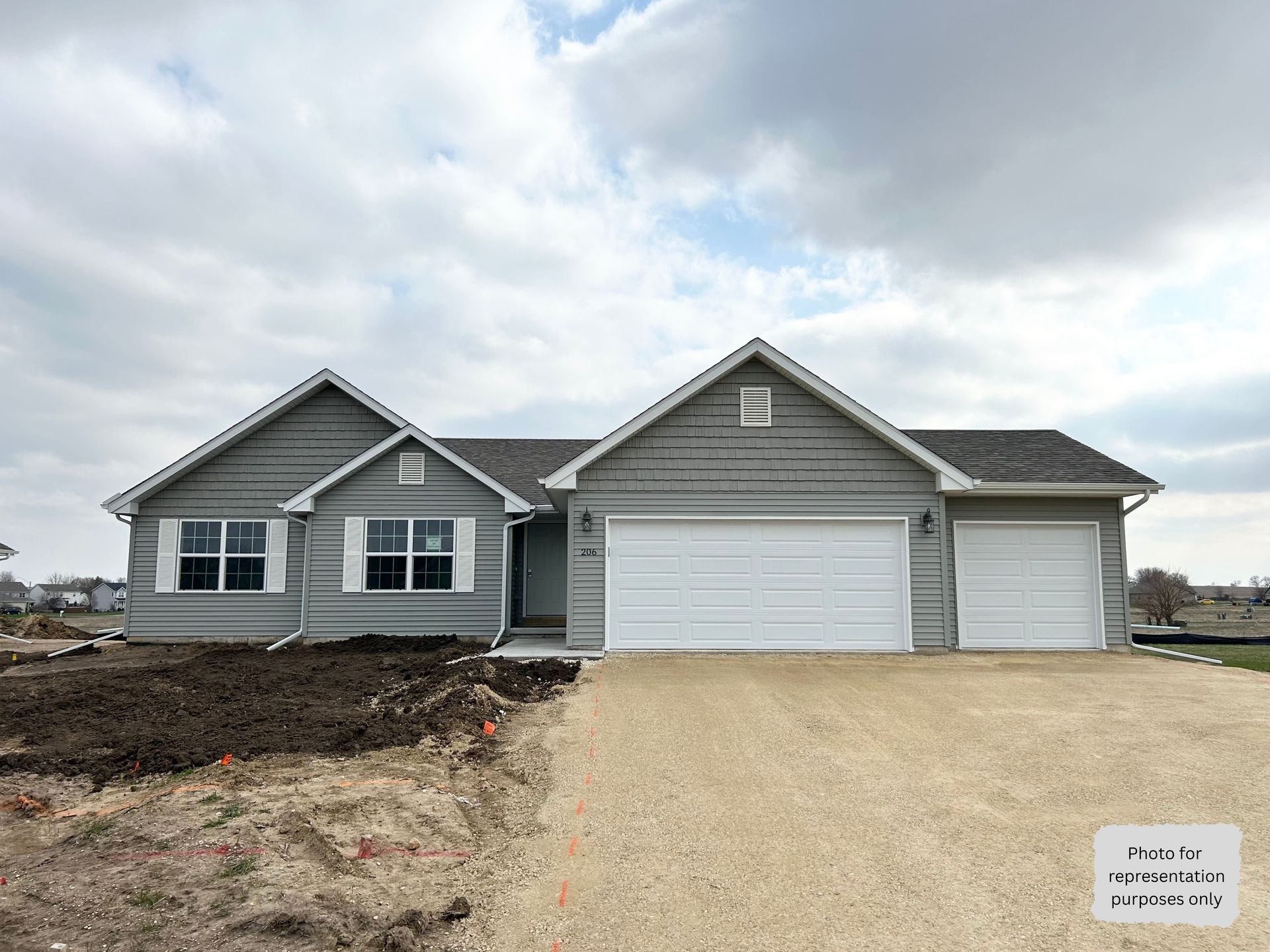 Gray house with white garage doors, under a cloudy sky, in a construction site.
