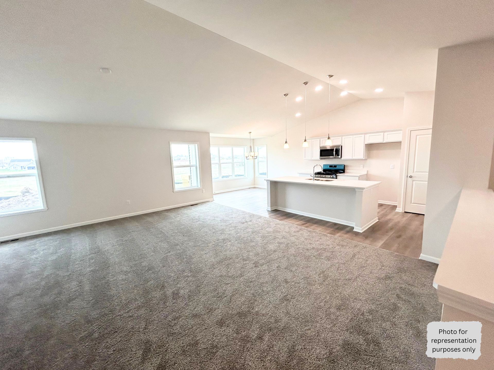 Spacious, open-concept living area with white walls, vaulted ceilings, gray carpet, and a modern white kitchen.