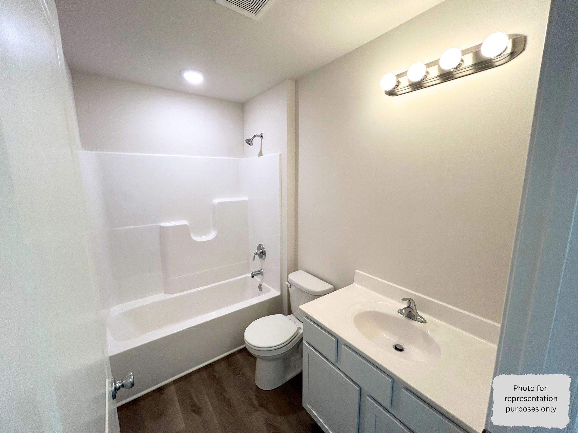 Bathroom with white tub/shower, toilet, vanity, and wood-look floor. Light gray walls.