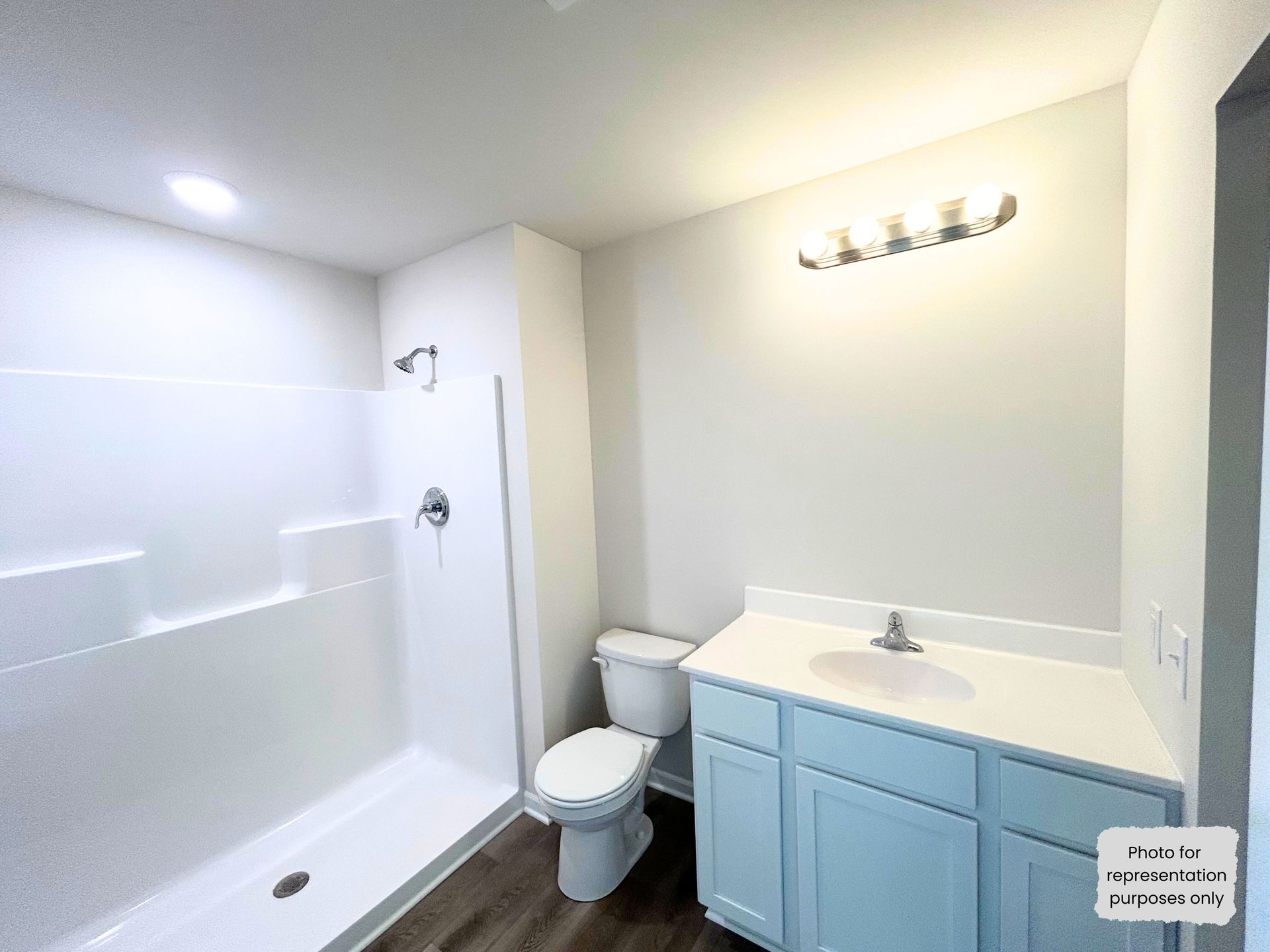 Bathroom with white shower, blue vanity, toilet, and light fixture on the wall.