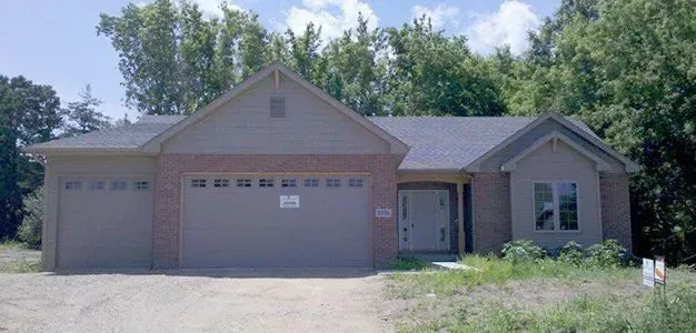 Ranch-style house with two-car garage, brick and siding exterior, surrounded by greenery and trees.