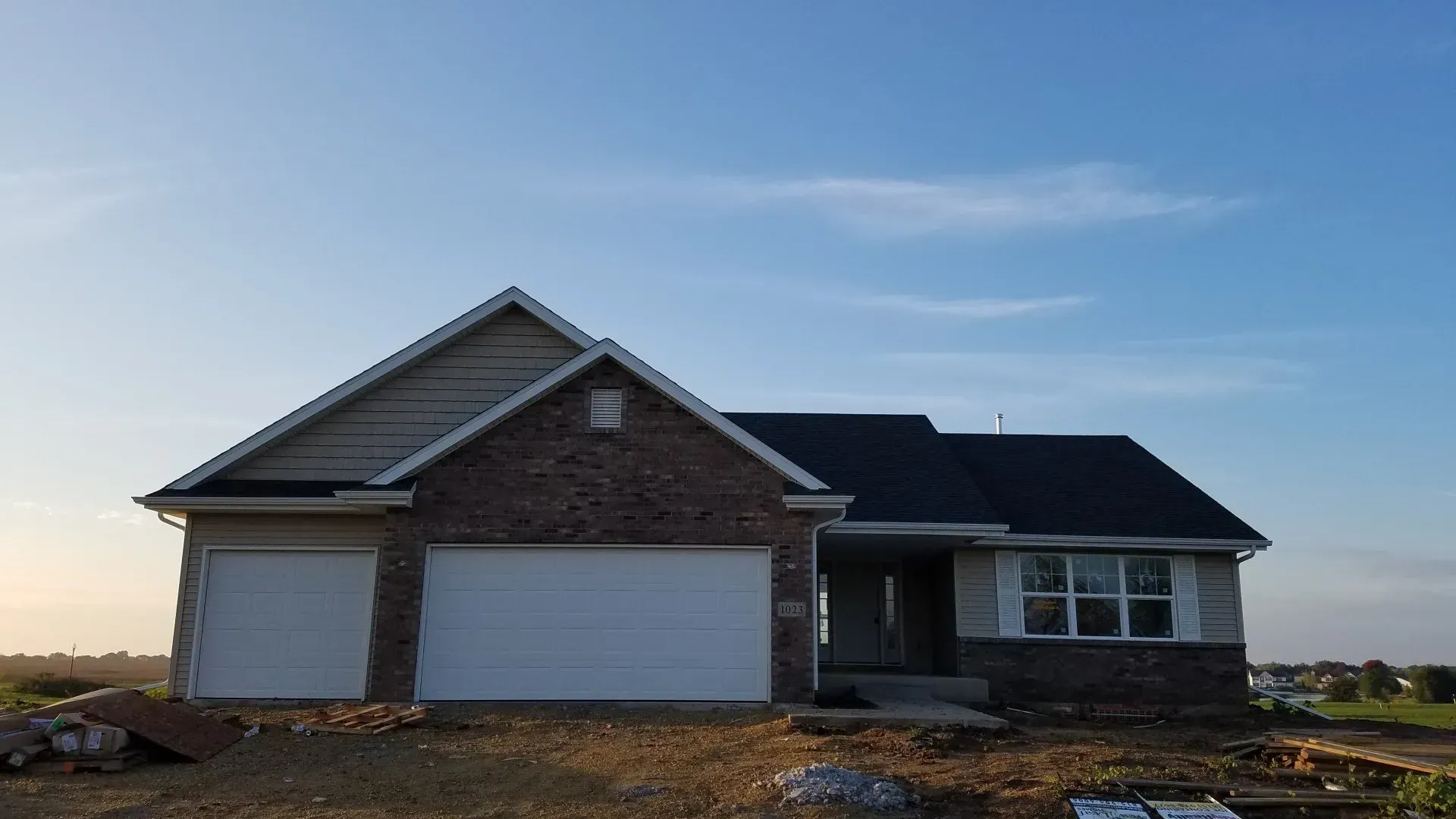 A new brick home with a two-car garage under a blue sky.