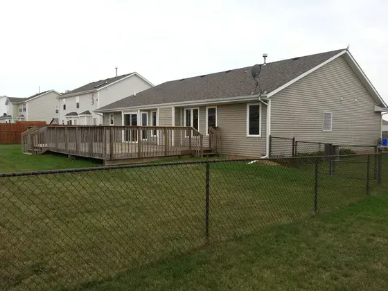 Backyard of a house with a wooden deck, fenced yard, and adjacent houses under an overcast sky.