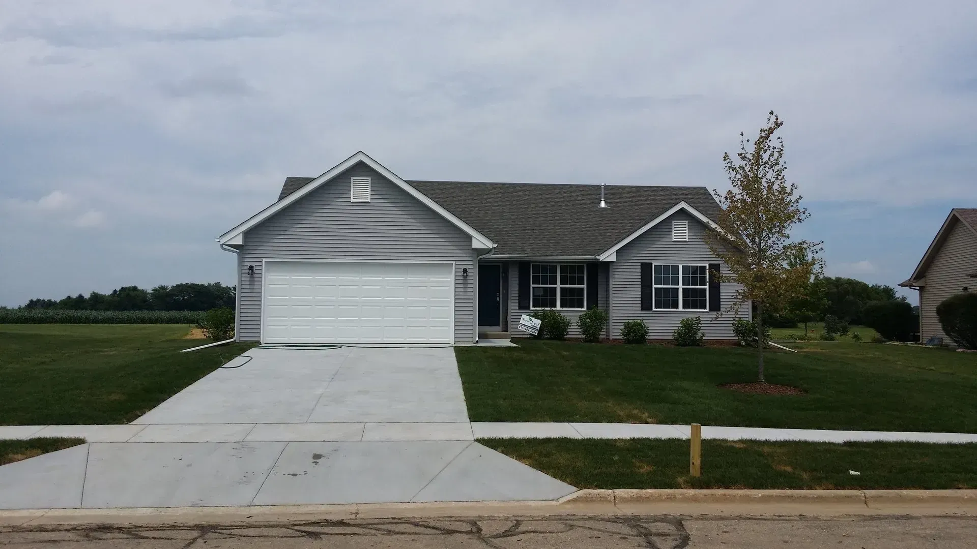 Gray house with attached garage, concrete driveway, and green lawn under a cloudy sky.