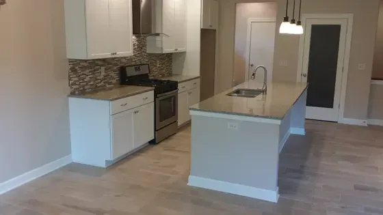 Modern white kitchen with island, stainless steel appliances, and light-colored cabinets.