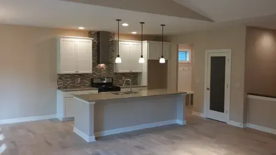 Kitchen with white cabinets, island, and pendant lights; neutral tones and wood flooring.