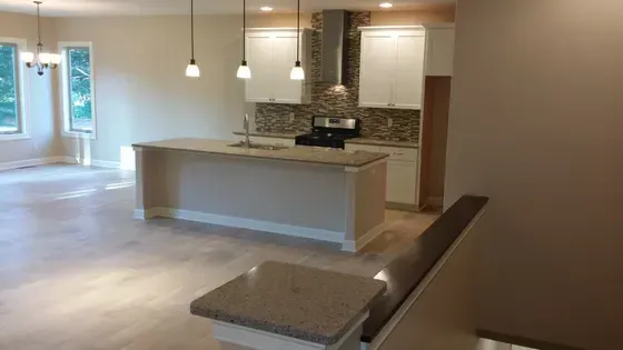 Modern kitchen with island and stovetop, light cabinets, and pendant lights.