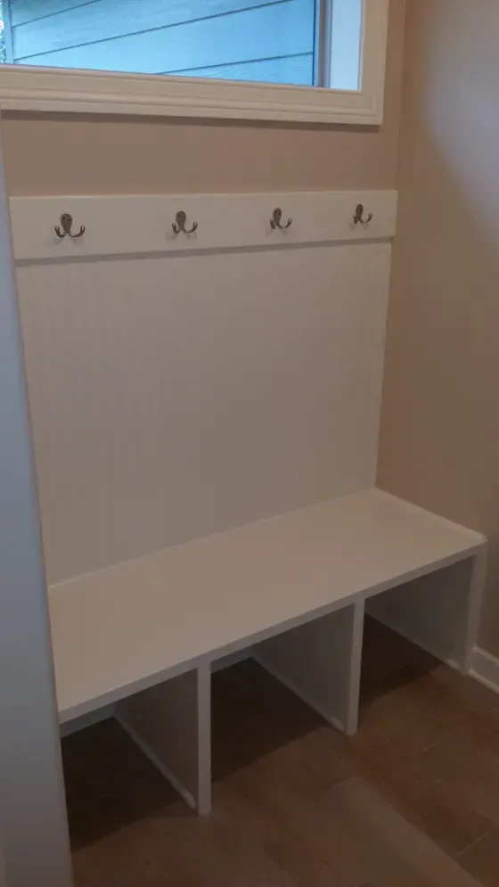 White built-in entryway bench with hooks, tan walls, and a window.